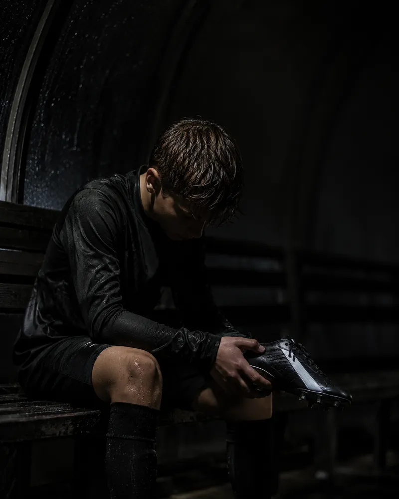 Young soccer player sitting alone in a dimly lit dugout, head bowed